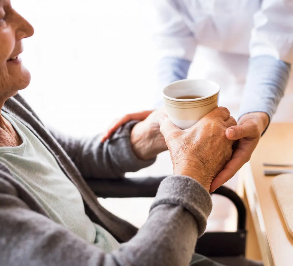Caregiver handing a Senior-aged woman a cup of tea Caregiver handing a Senior-aged woman a cup of tea