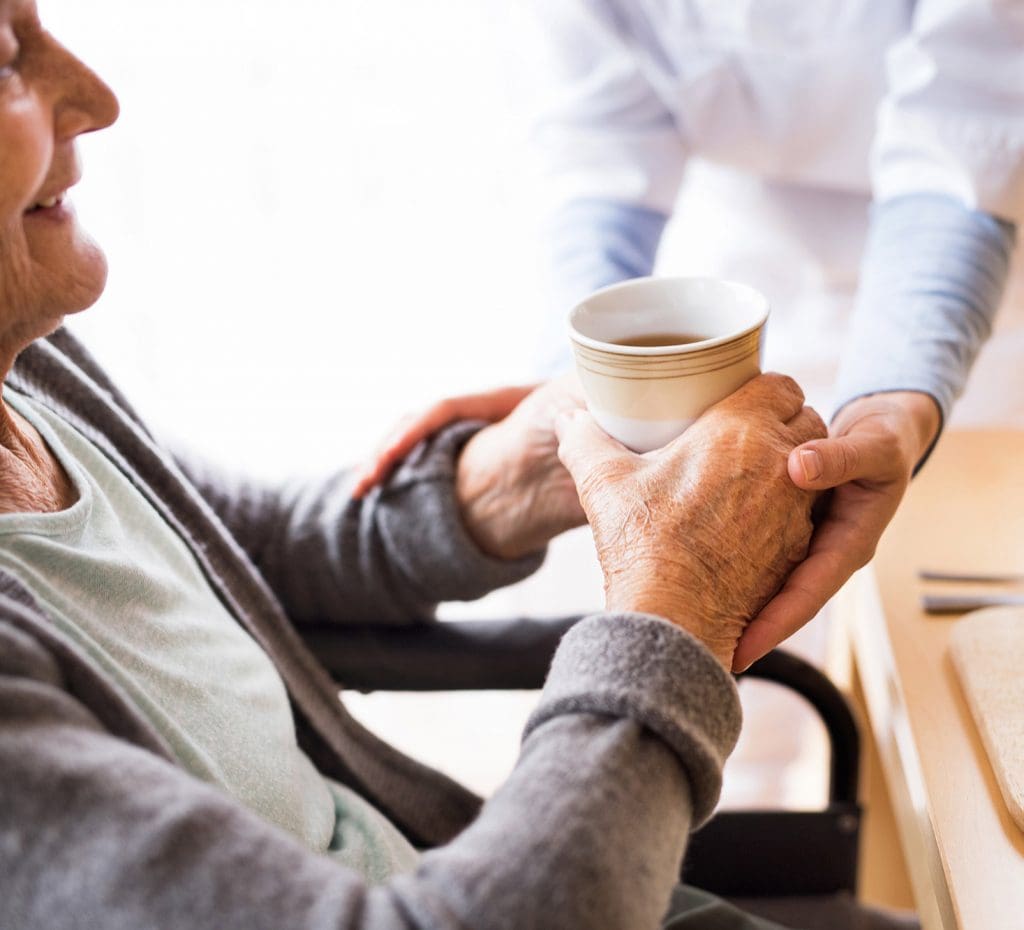 Caregiver handing a Senior-aged woman a cup of tea