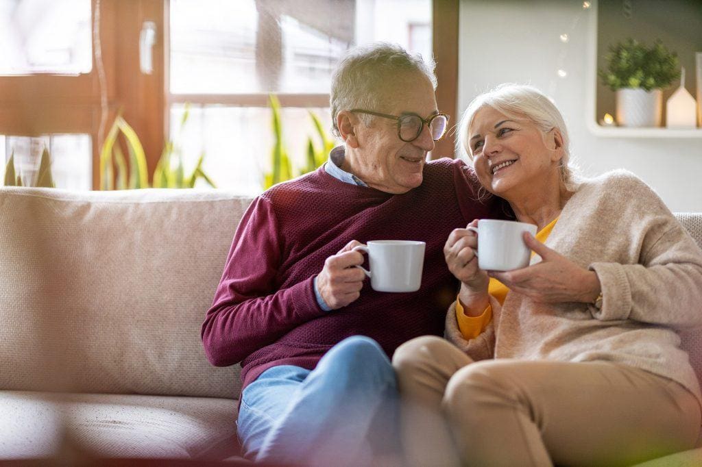 Elderly couple drinking coffee together on the sofa at home