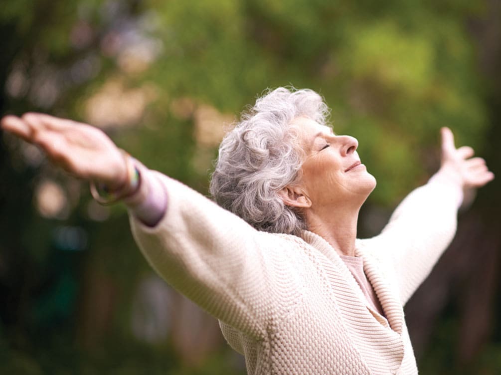 Senior woman lifting her arms to the sky with her eyes closed