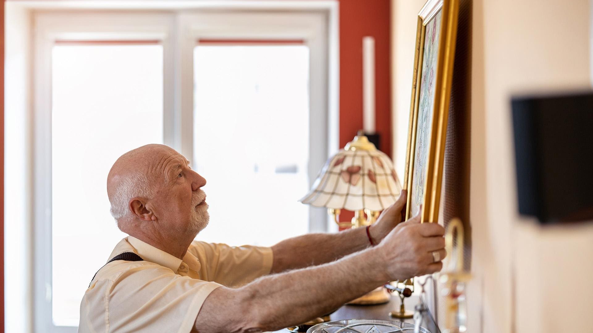 Senior man putting up a painting on the wall at his home