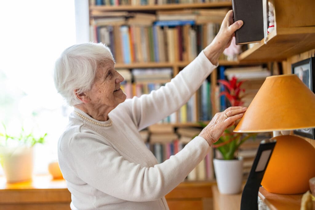 Senior woman selecting book from bookshelf at home